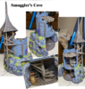 A painted 3D print of the Smuggler's Cove terrain, featuring a ruined gray stone tower built upon a mossy rock cliff. A wooden scaffolding and a pointed wooden roof adorn the tower. A hidden cave in the cliff reveals a detailed interior with wooden stairs, shelves of bottles, and a barrel.