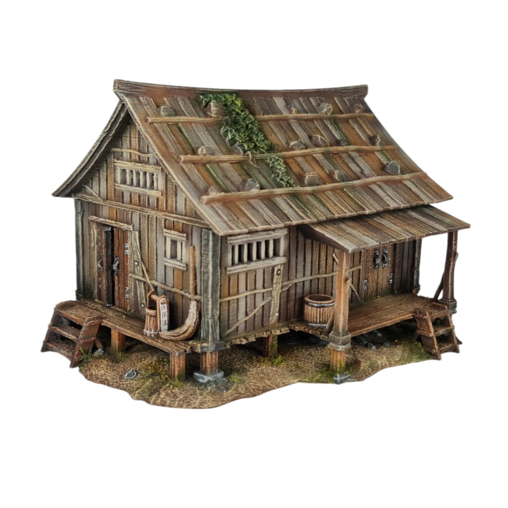 A 28mm scale 3D printed model of an Ishioki-Minka, a traditional Japanese mountain farmhouse. The structure features a unique roof made of flat wooden planks weighted down by numerous realistic stones, a raised timber porch (Engawa) with steps, and weathered wood-grain siding, all set on a stone-pillared foundation.
