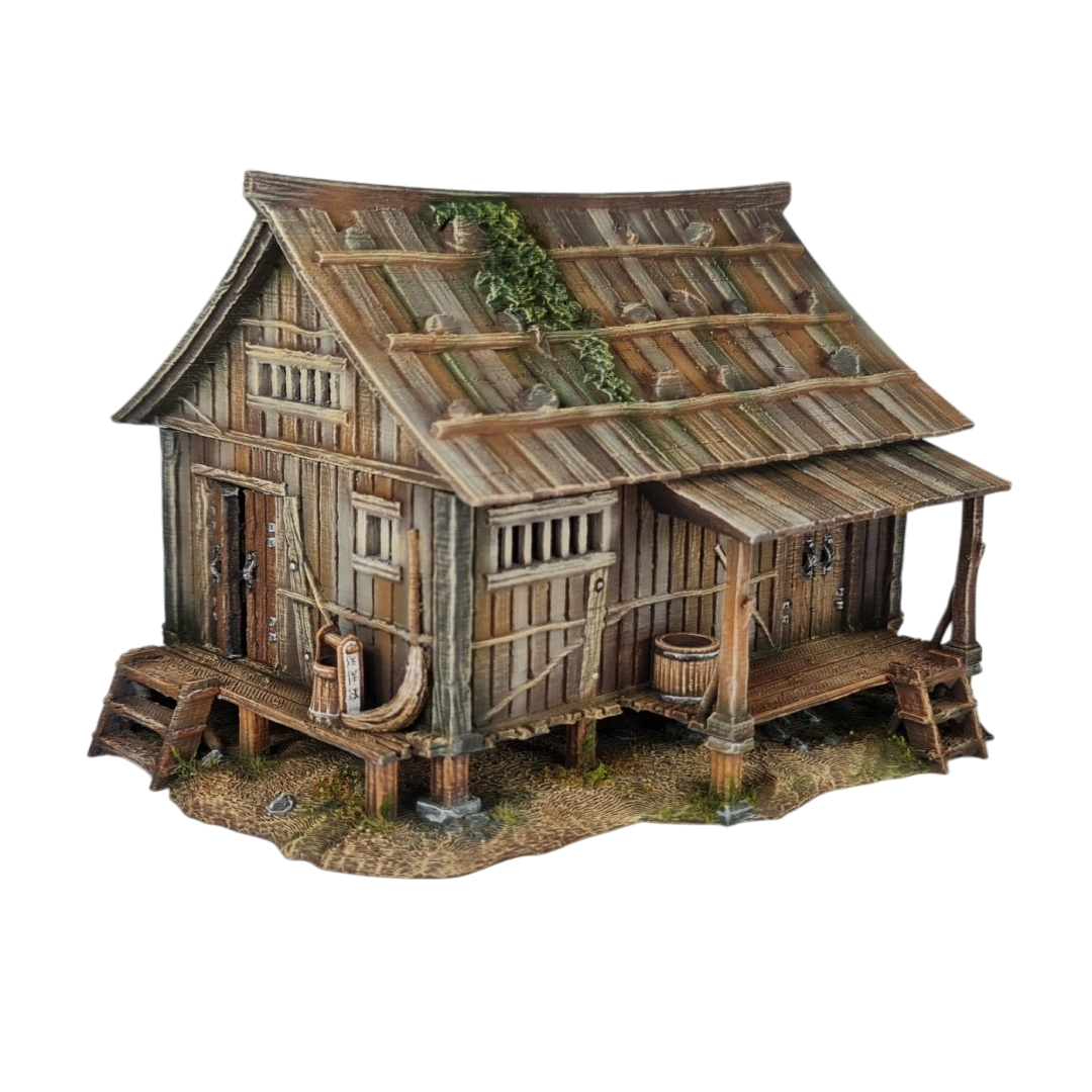 A 28mm scale 3D printed model of an Ishioki-Minka, a traditional Japanese mountain farmhouse. The structure features a unique roof made of flat wooden planks weighted down by numerous realistic stones, a raised timber porch (Engawa) with steps, and weathered wood-grain siding, all set on a stone-pillared foundation.