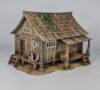 A 28mm scale 3D printed model of an Ishioki-Minka, a traditional Japanese mountain farmhouse. The structure features a unique roof made of flat wooden planks weighted down by numerous realistic stones, a raised timber porch (Engawa) with steps, and weathered wood-grain siding, all set on a stone-pillared foundation.