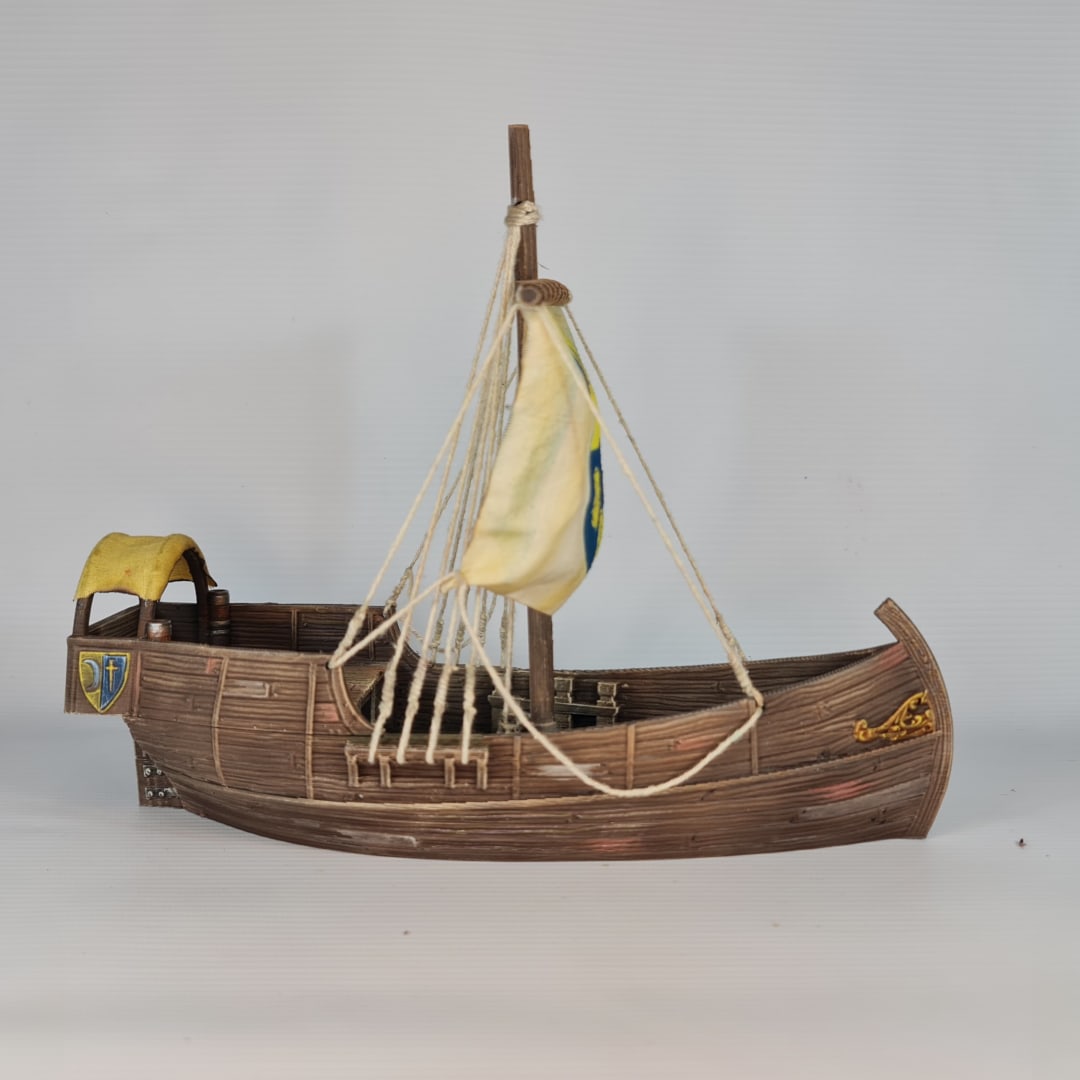 3D printed and painted model of a medieval merchant cog ship, front view. The ship has a detailed wooden hull, a single mast, and a square sail with a blue and yellow coat of arms.