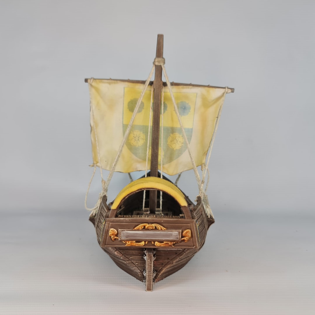 3D printed and painted model of a medieval merchant cog ship, front view. The ship has a detailed wooden hull, a single mast, and a square sail with a blue and yellow coat of arms.