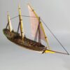 Painted 28mm scale model of a historical Xebec ship, featuring three masts with lateen sails, a wooden deck with cannons, and miniatures for scale.