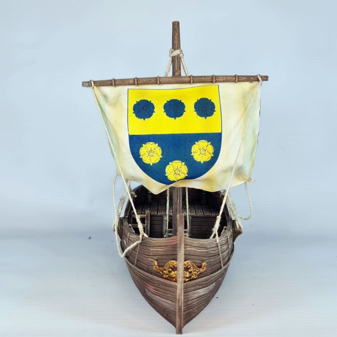 3D printed and painted model of a medieval merchant cog ship, front view. The ship has a detailed wooden hull, a single mast, and a square sail with a blue and yellow coat of arms.