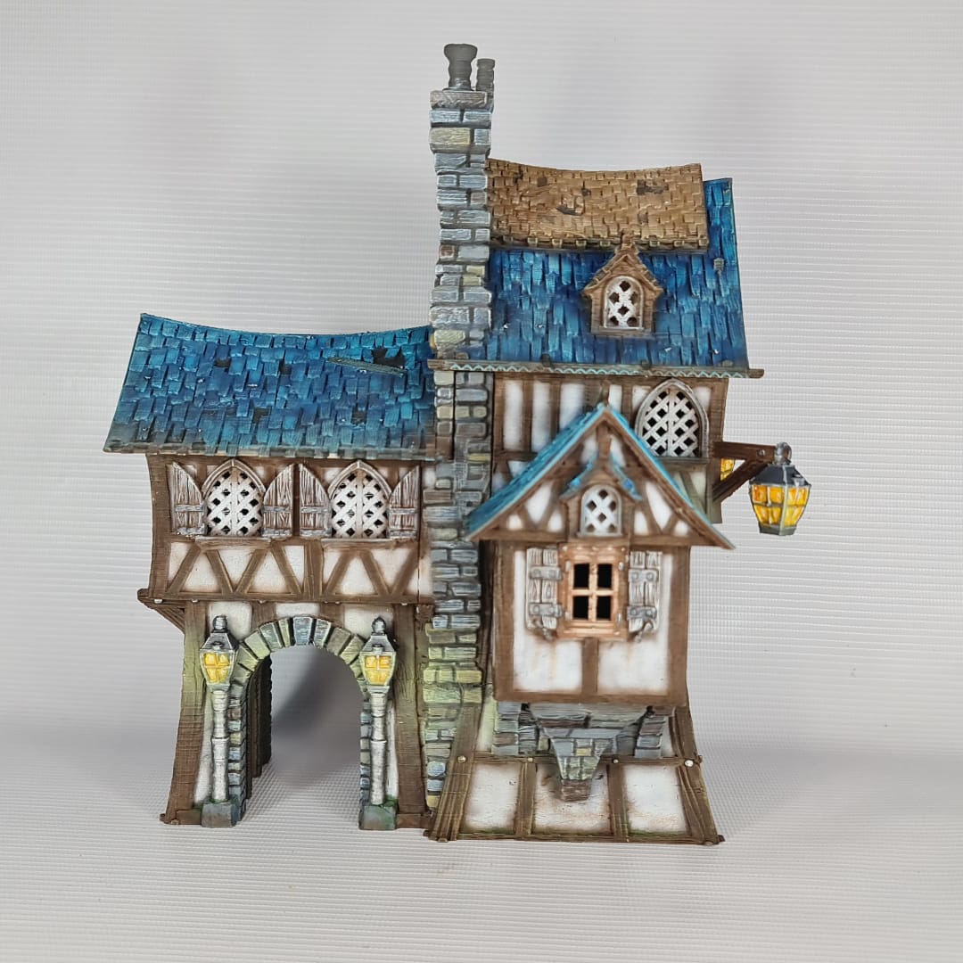 3D printed and painted model of the Oldkeep Barracks, a medieval half-timbered building with blue shingled roofs, hanging lanterns, and wooden textures for tabletop gaming.