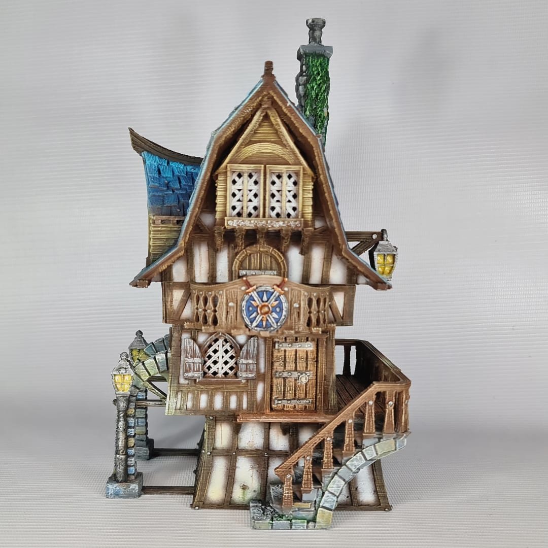 3D printed and painted model of a multi-story medieval fantasy house featuring half-timbered walls, a steep blue roof, stone pillars with lamps, and an external wooden staircase.