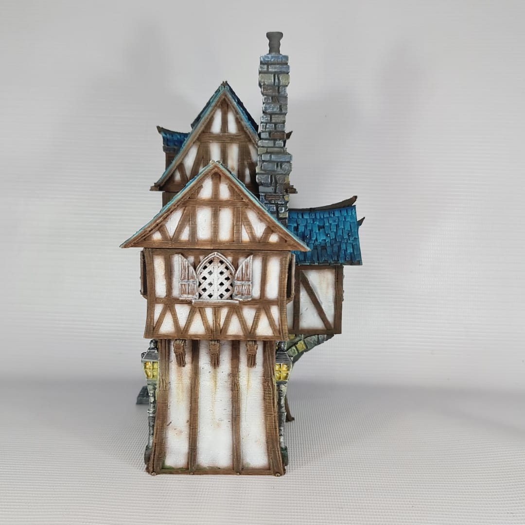 3D printed and painted model of the Oldkeep Barracks, a medieval half-timbered building with blue shingled roofs, hanging lanterns, and wooden textures for tabletop gaming.
