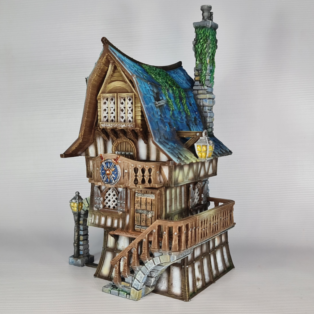 3D printed and painted model of a multi-story medieval fantasy house featuring half-timbered walls, a steep blue roof, stone pillars with lamps, and an external wooden staircase.