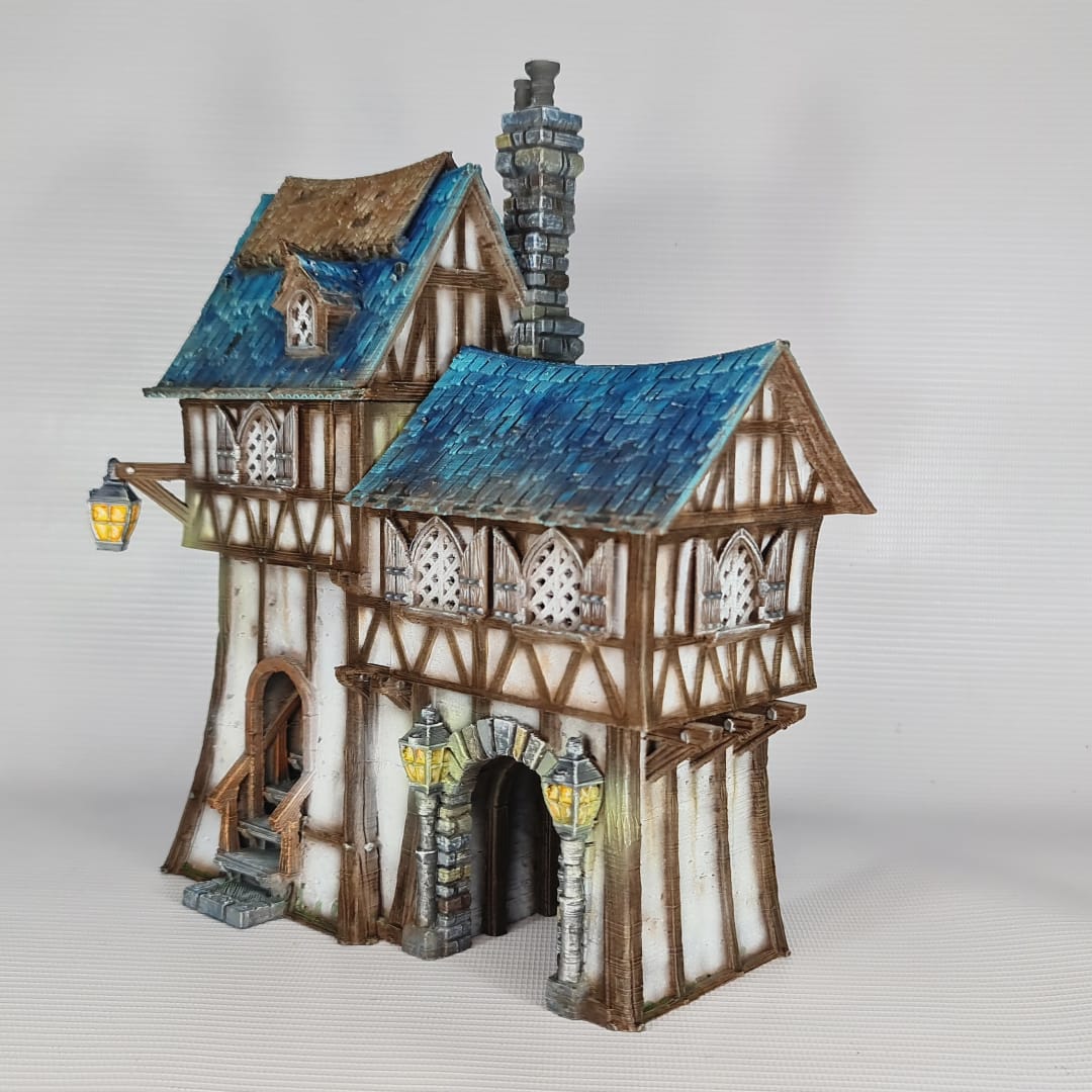 3D printed and painted model of the Oldkeep Barracks, a medieval half-timbered building with blue shingled roofs, hanging lanterns, and wooden textures for tabletop gaming.