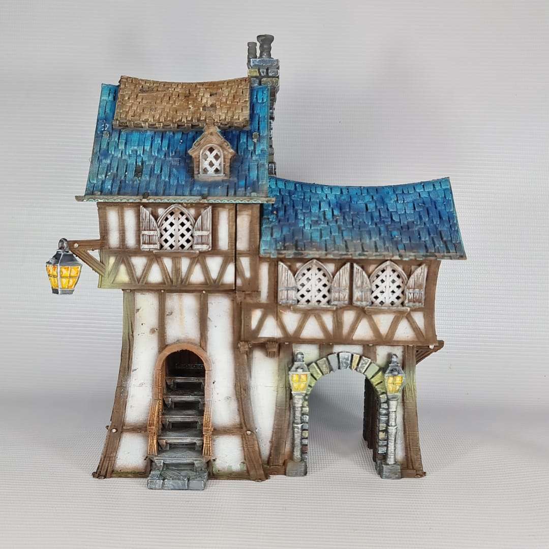 3D printed and painted model of the Oldkeep Barracks, a medieval half-timbered building with blue shingled roofs, hanging lanterns, and wooden textures for tabletop gaming.