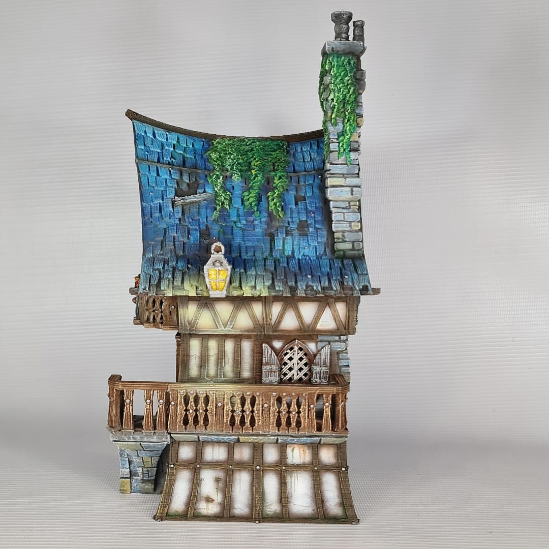 3D printed and painted model of a multi-story medieval fantasy house featuring half-timbered walls, a steep blue roof, stone pillars with lamps, and an external wooden staircase.