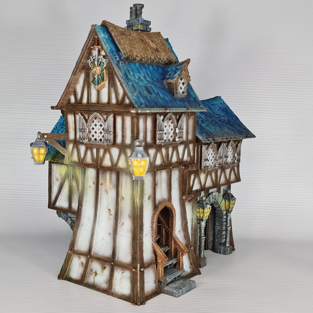 3D printed and painted model of the Oldkeep Barracks, a medieval half-timbered building with blue shingled roofs, hanging lanterns, and wooden textures for tabletop gaming.