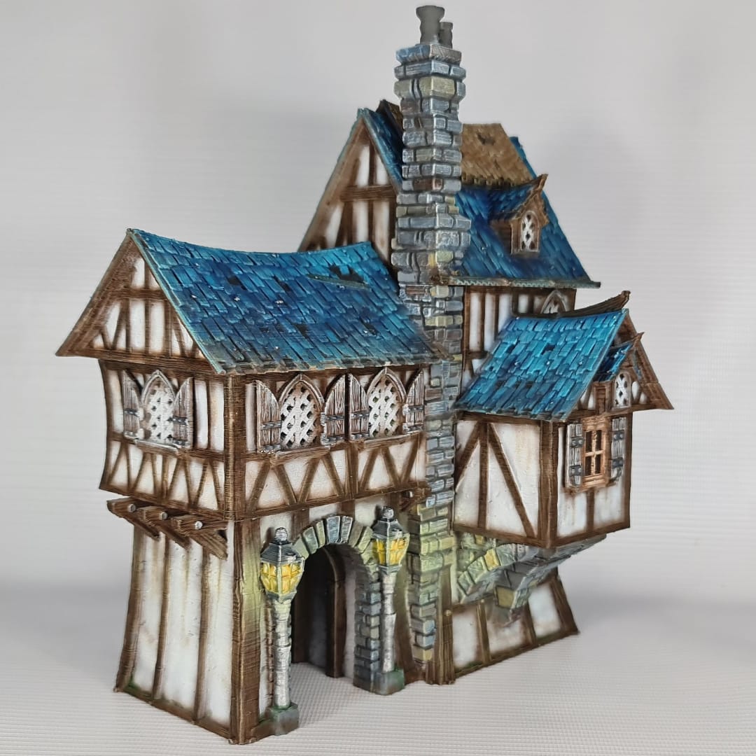 3D printed and painted model of the Oldkeep Barracks, a medieval half-timbered building with blue shingled roofs, hanging lanterns, and wooden textures for tabletop gaming.