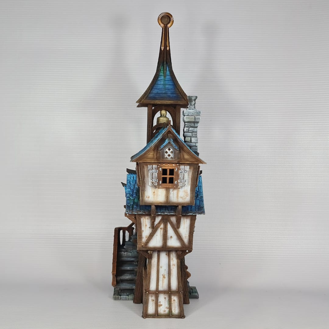 3D printed and painted model of Parson's Lodge, a tall medieval fantasy bell tower with half-timbered walls, blue shingled roofs, stone chimney, and wooden stairs.
