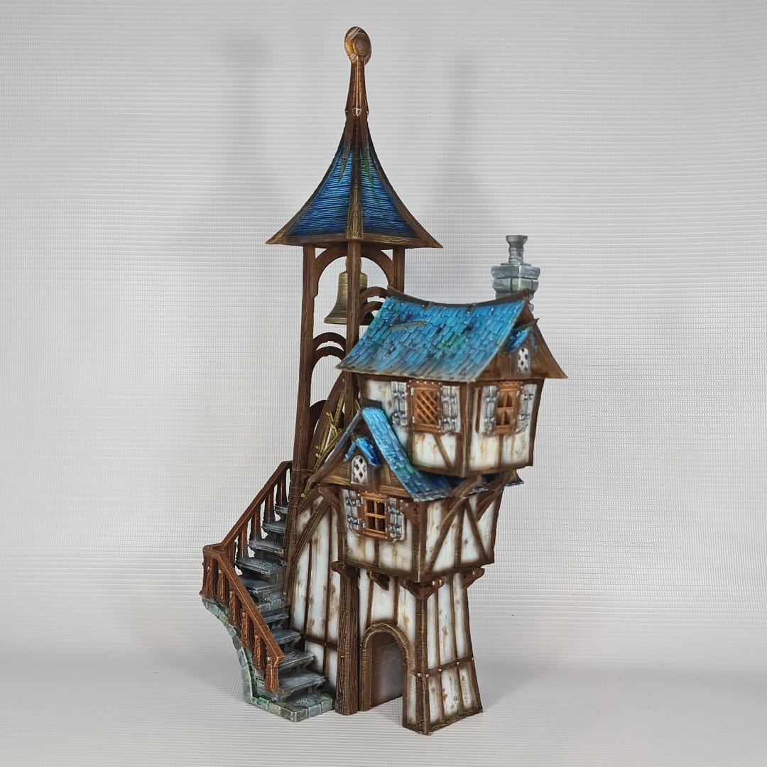 3D printed and painted model of Parson's Lodge, a tall medieval fantasy bell tower with half-timbered walls, blue shingled roofs, stone chimney, and wooden stairs.