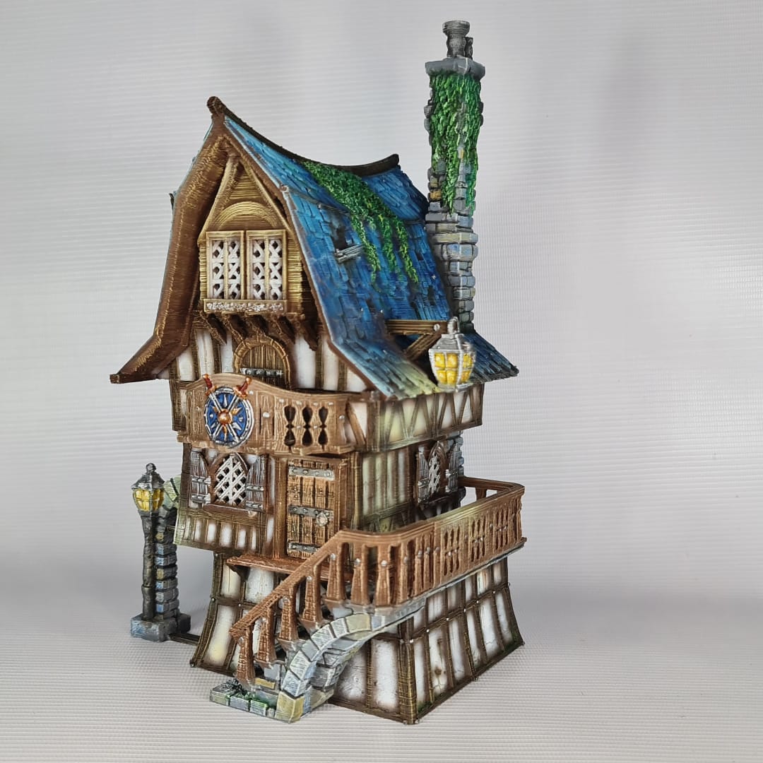3D printed and painted model of a multi-story medieval fantasy house featuring half-timbered walls, a steep blue roof, stone pillars with lamps, and an external wooden staircase.