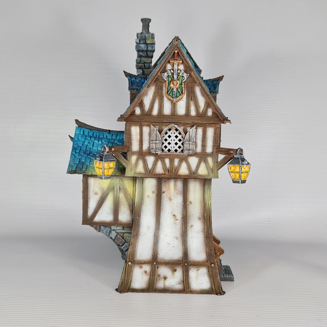 3D printed and painted model of the Oldkeep Barracks, a medieval half-timbered building with blue shingled roofs, hanging lanterns, and wooden textures for tabletop gaming.