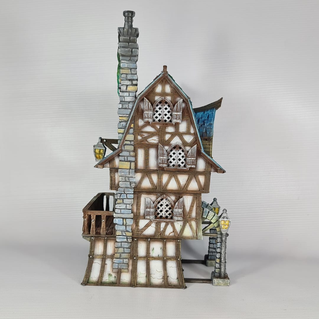 3D printed and painted model of a multi-story medieval fantasy house featuring half-timbered walls, a steep blue roof, stone pillars with lamps, and an external wooden staircase.